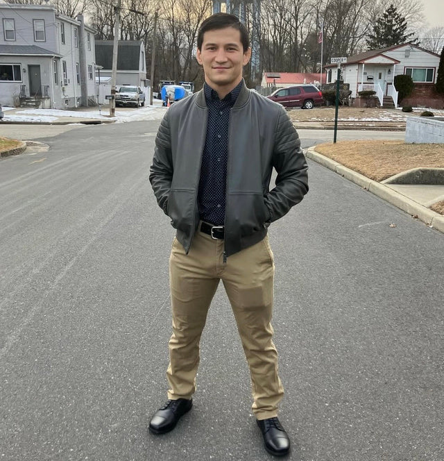 A man in a grey leather bomber jacket standing on a suburban street wearing black leather Birchbury oxfords